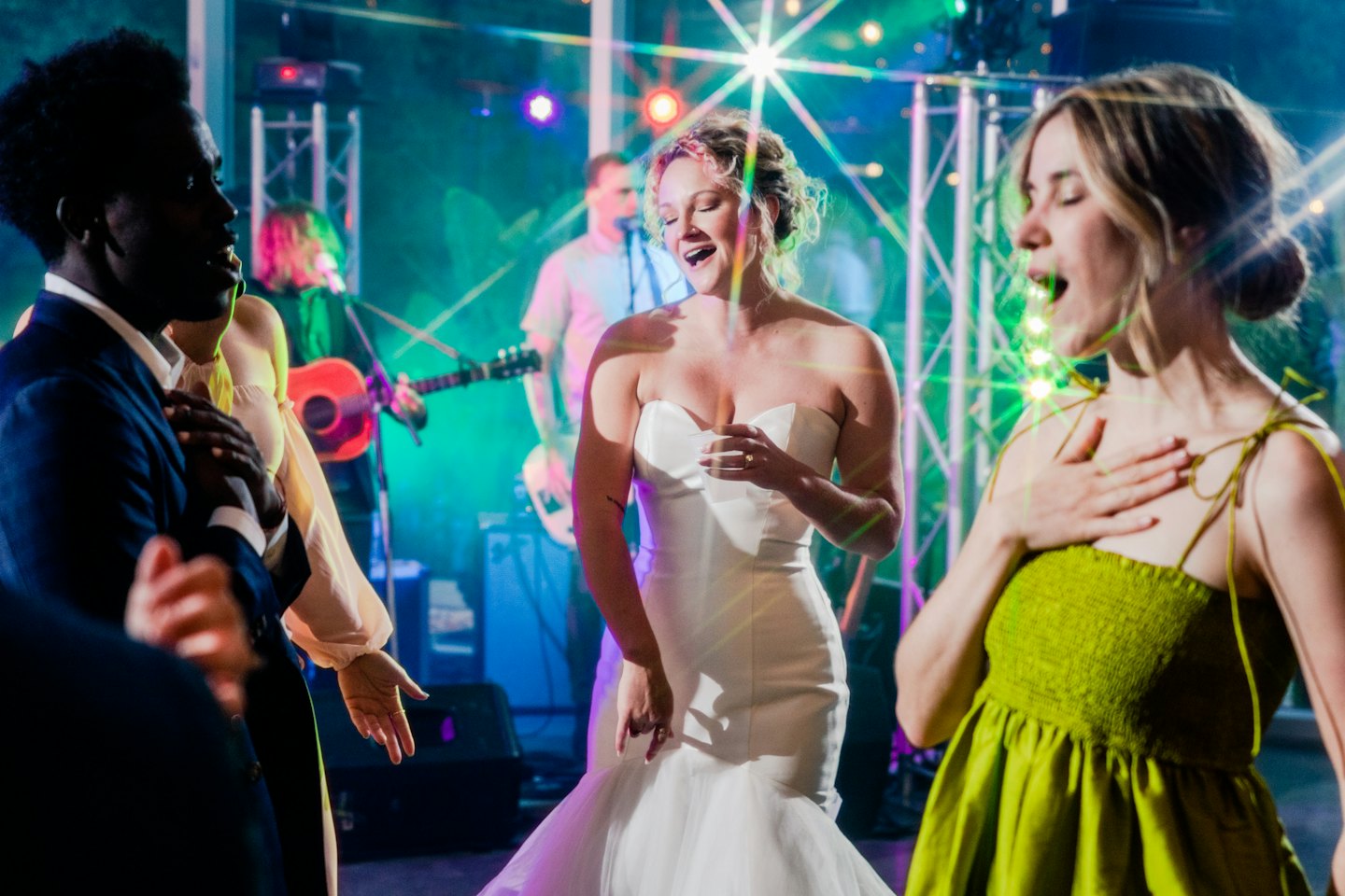 Wedding guests joyfully dance and sing near a bride in a white gown.