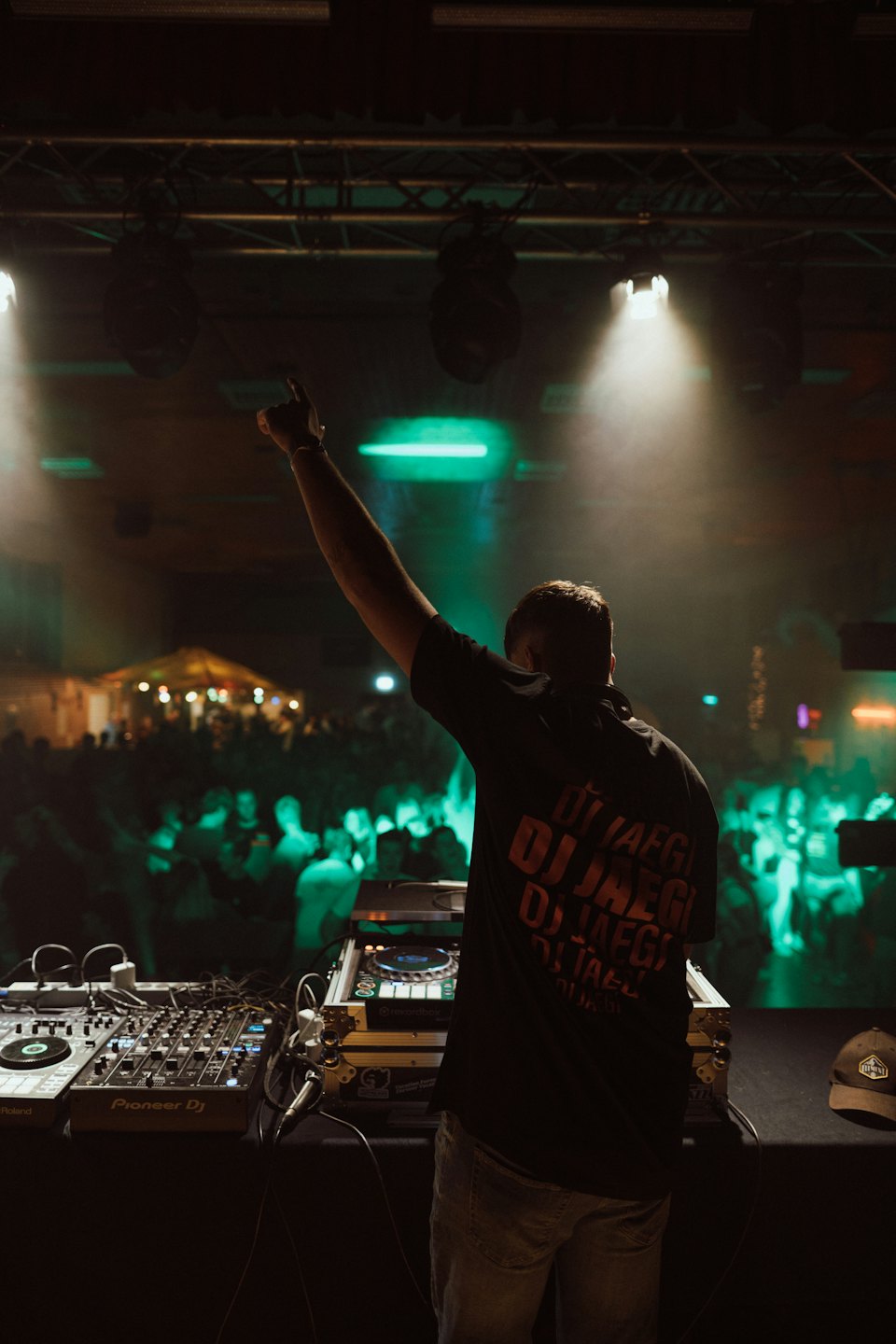 DJ with arm raised above sound equipment at a night event.